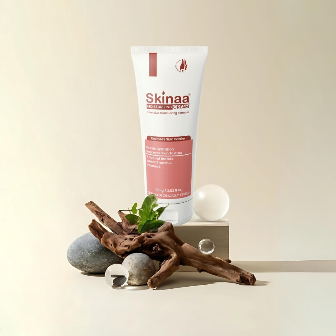 Skinaa Moisturizing Cream tube for dry skin type, made with 5 natural butters and wheat protein, placed upright on a beige background with stones, wooden branches, and green leaves for an organic look.
